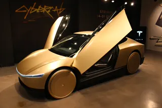 Gold Tesla Cybercab displayed indoors with both doors raised.