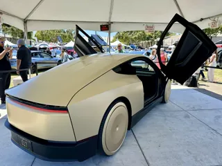 Rear three-quarter view of a gold Tesla Cybercab under an event canopy, with doors raised.